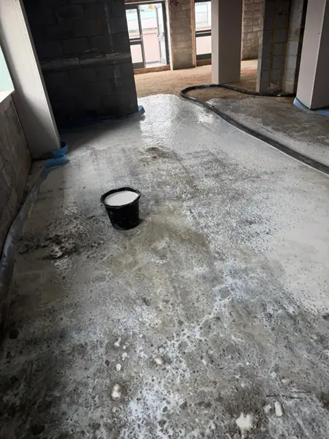 Bonding agent brushed across a prepared concrete slab, with a bucket of bonding slurry ready for the screed
