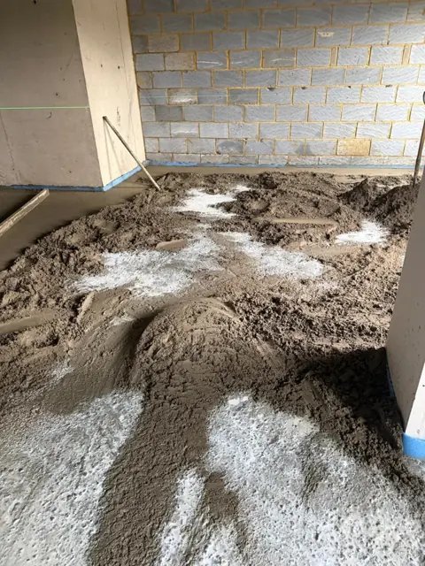 Sand and cement screed being laid onto a wet bonding coat