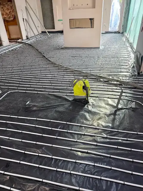 Underfloor heating pipes laid over black membrane with a site level on the floor