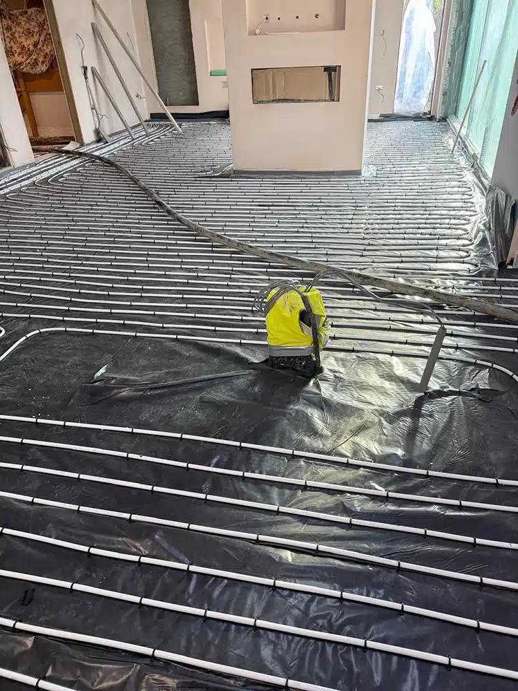 Underfloor heating pipes laid over black membrane with a site level on the floor